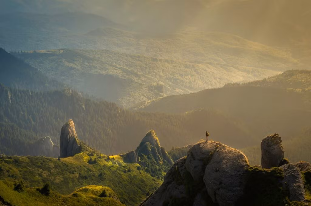 A person sitting on a rocky outcrop overlooking a mountainous landscape with a valley below, shrouded in mist.